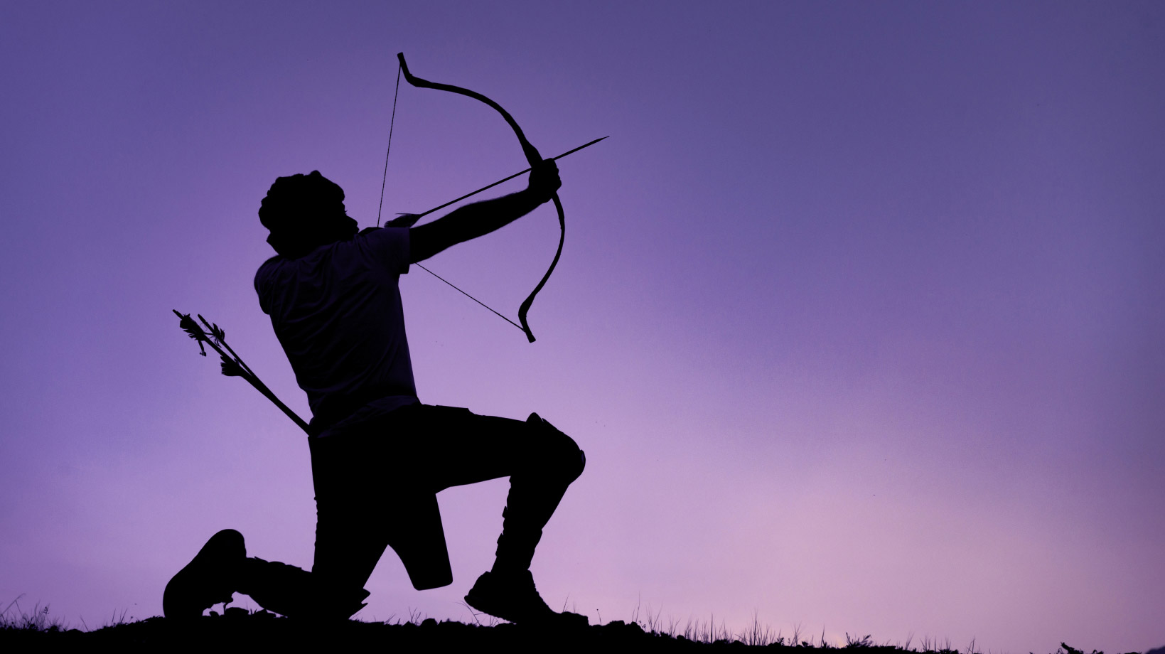 silhouette of an archer on his knee drawing his bow