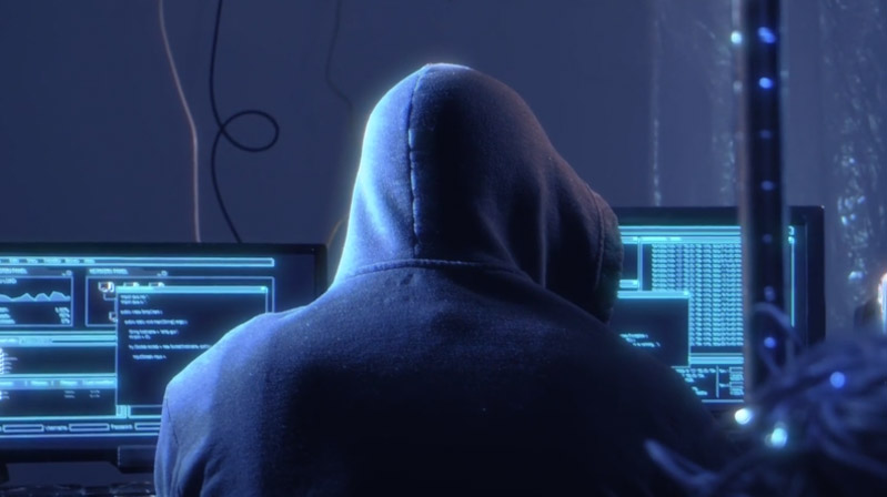 hooded hacker working on multiple computers